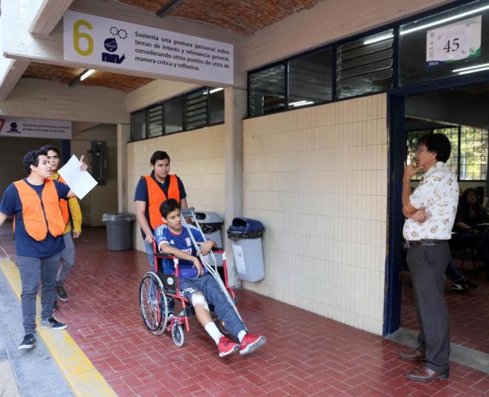 Aspirante en silla de ruedas trasladándose hacia su salón para aplicar el examen de admisión