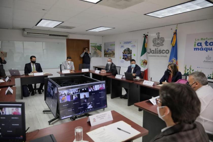 Siete personas sentadas al rededor de cuatro televisores, están en una videollamada.