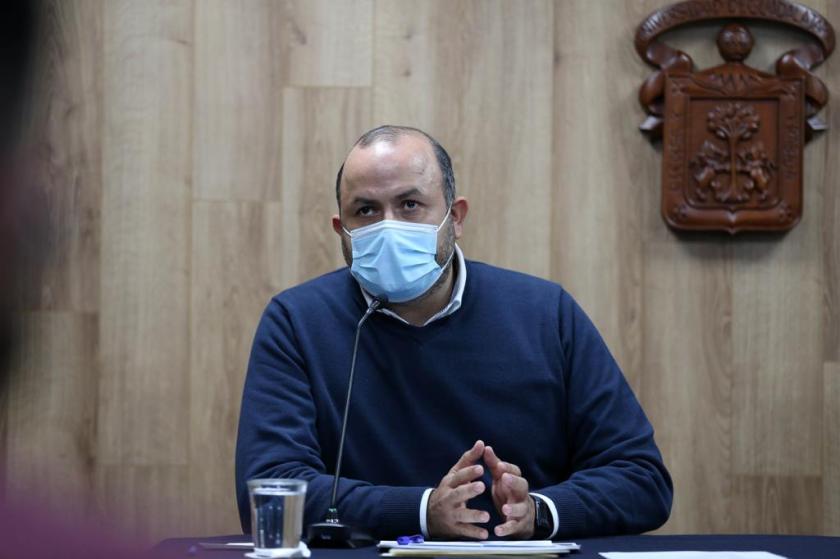 Una persona sentada detrás de un escritorio, frente a él hay un micrófono.  