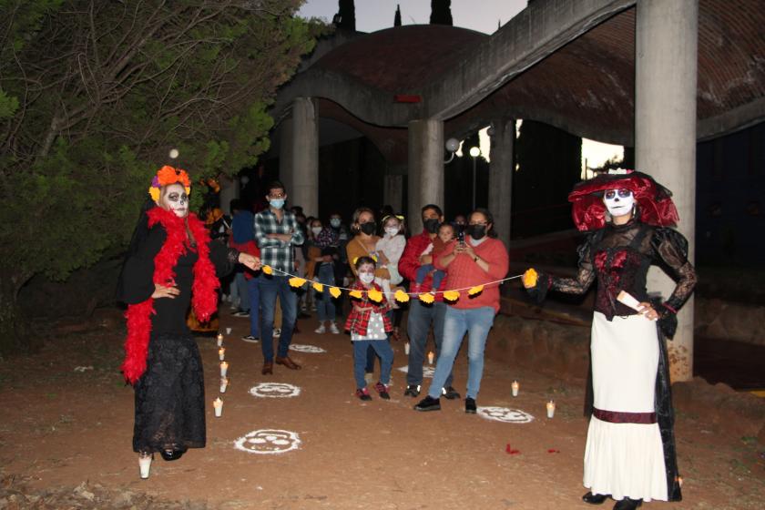 Alumnas caracterizadas de catrinas sostienen un hilo de flores frente a público.