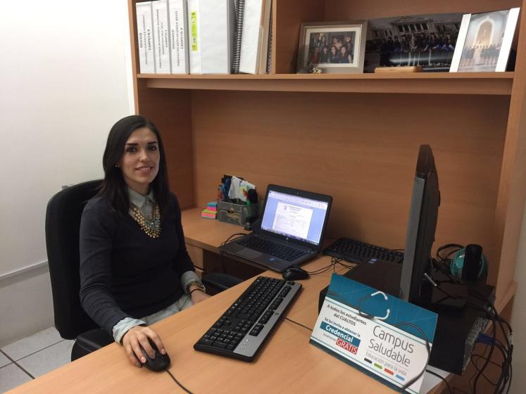 Persona sentada viedo a la cámara, frente a ella un escritorio.
