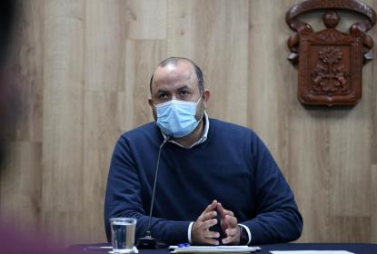 Una persona sentada detrás de un escritorio, frente a él hay un micrófono.  